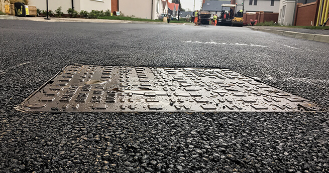 Manhole Cover Installed by Mackoy Groundworks Operatives with Further Tarmac Works Going on in the Background