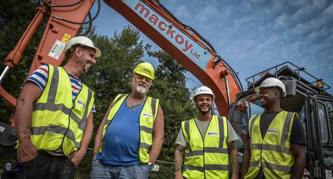 Four Groundworks Operatives in front of orange Mackoy Excavator